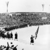 Олимпийские игры 1936, Гармиш-Партенкирхен. Члены олимпийской сборной США маршируют за американским флагом на заснеженном лыжном стадионе во время церемонии открытия IV зимних Олимпийских игр в Гармиш-Партенкирхене в Германии 6 февраля 1936 года. В играх приняли участие 668 спортсменов из 28 стран.